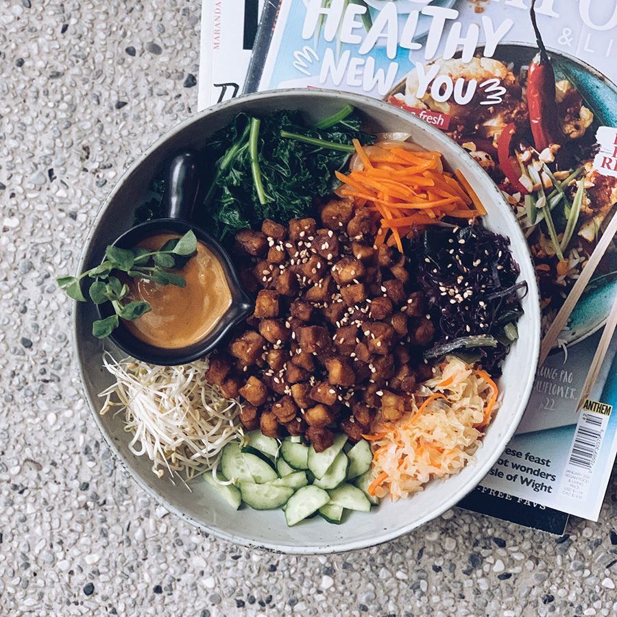 A buddha bowl next to chopsticks and a magazine