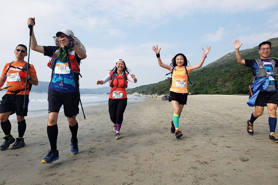  group of trail runners smile and wave while walking on a beach at the Barclays MoonTrekker