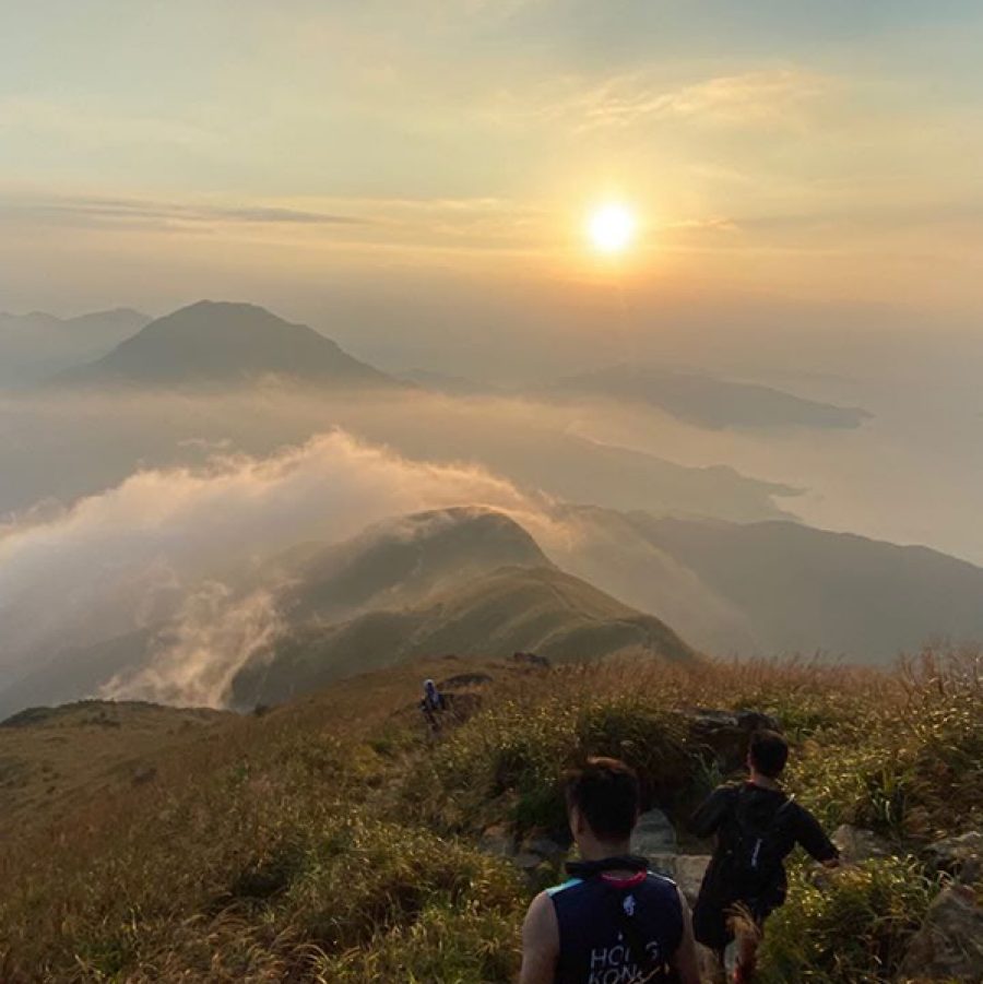 A group of people walking down the peak on a hiking trail at sunset 