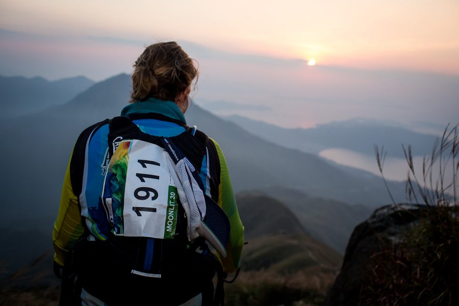 A woman trail runner standing on a hill watching the sunrise 