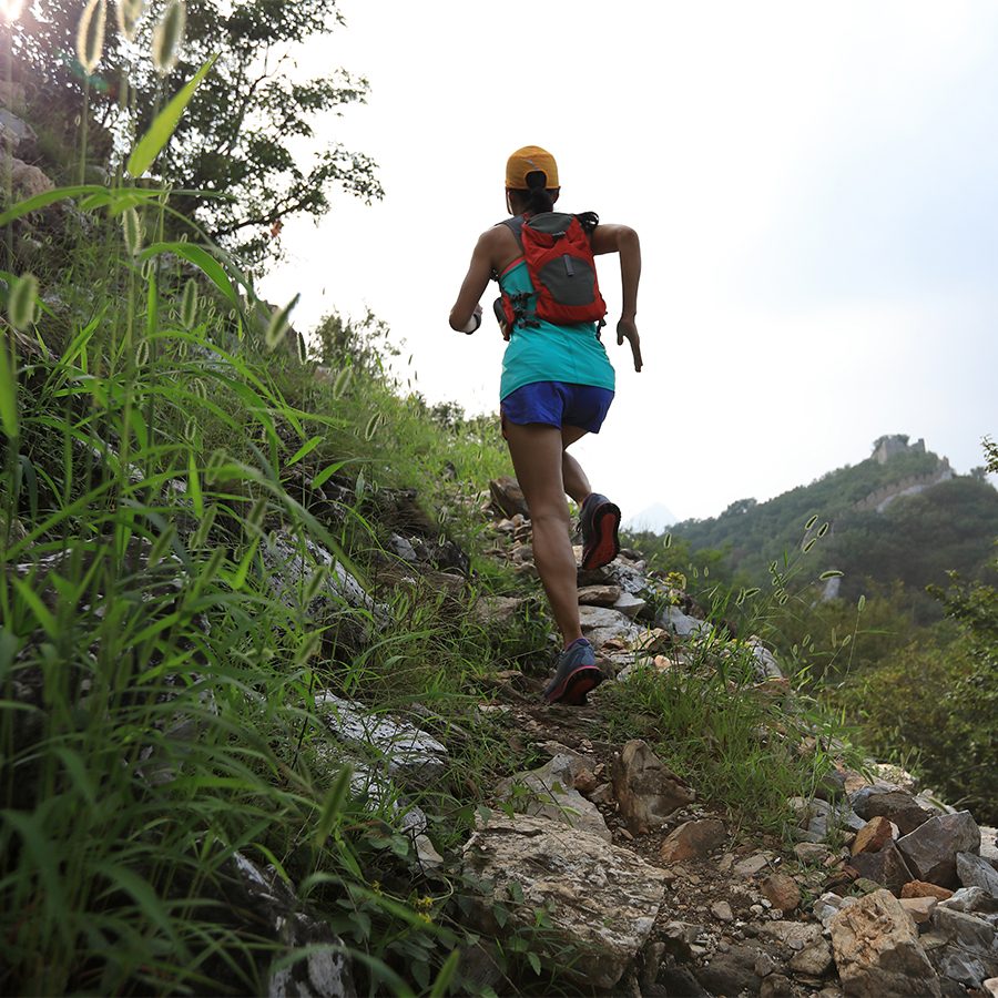 A woman running uphill on a rocky trail on a sunny day 