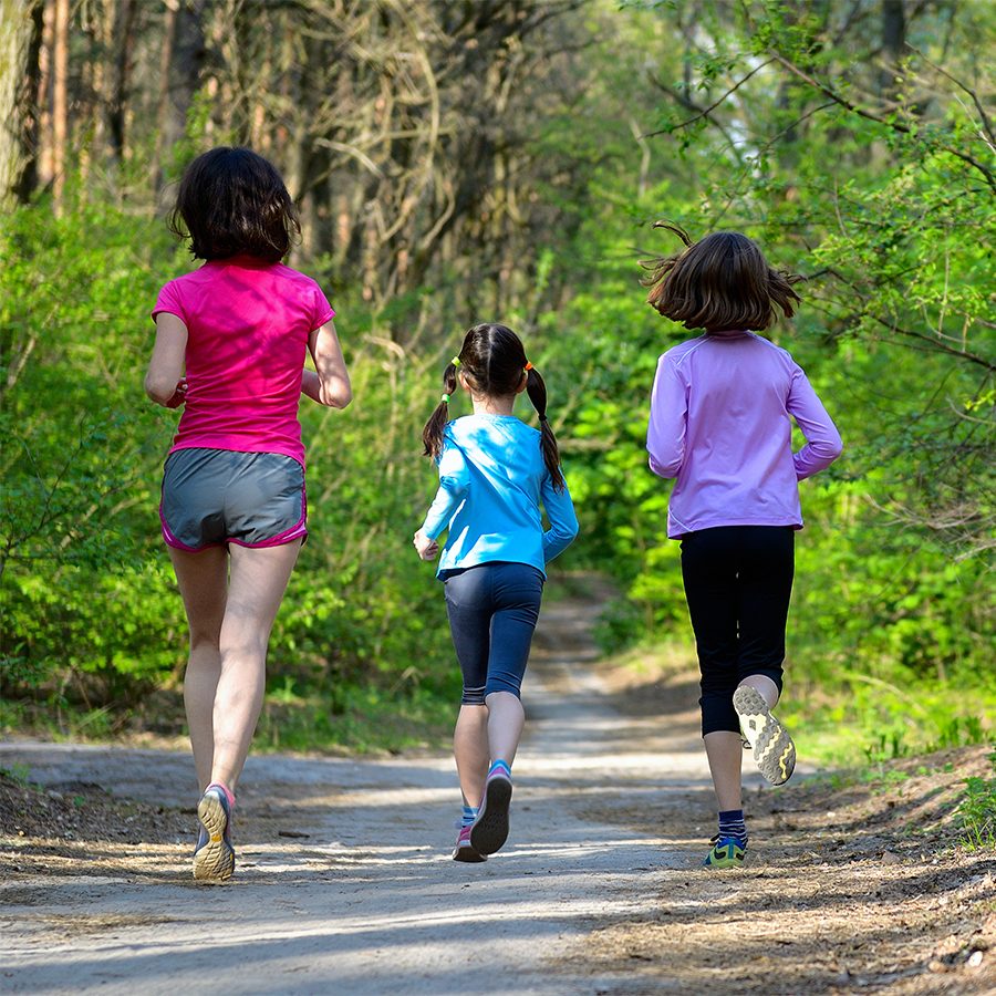 A family of a woman and two young girls running together in a forest