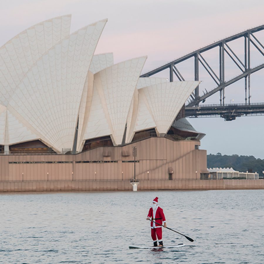Santa paddle boarding in front of the Sydney opera house and bridge