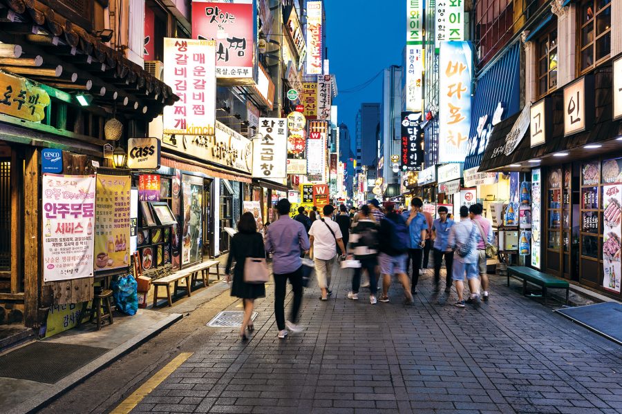 Pedestrians walk along a street full of restaurants in Seoul.