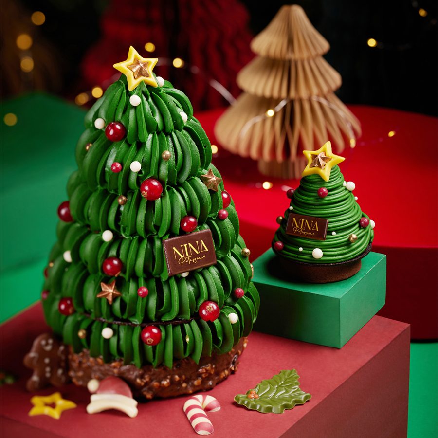 A close up of a small and a big Nina Patisserie Christmas tree-shaped pistachio chocolate cake on top of decorative red and green boxes