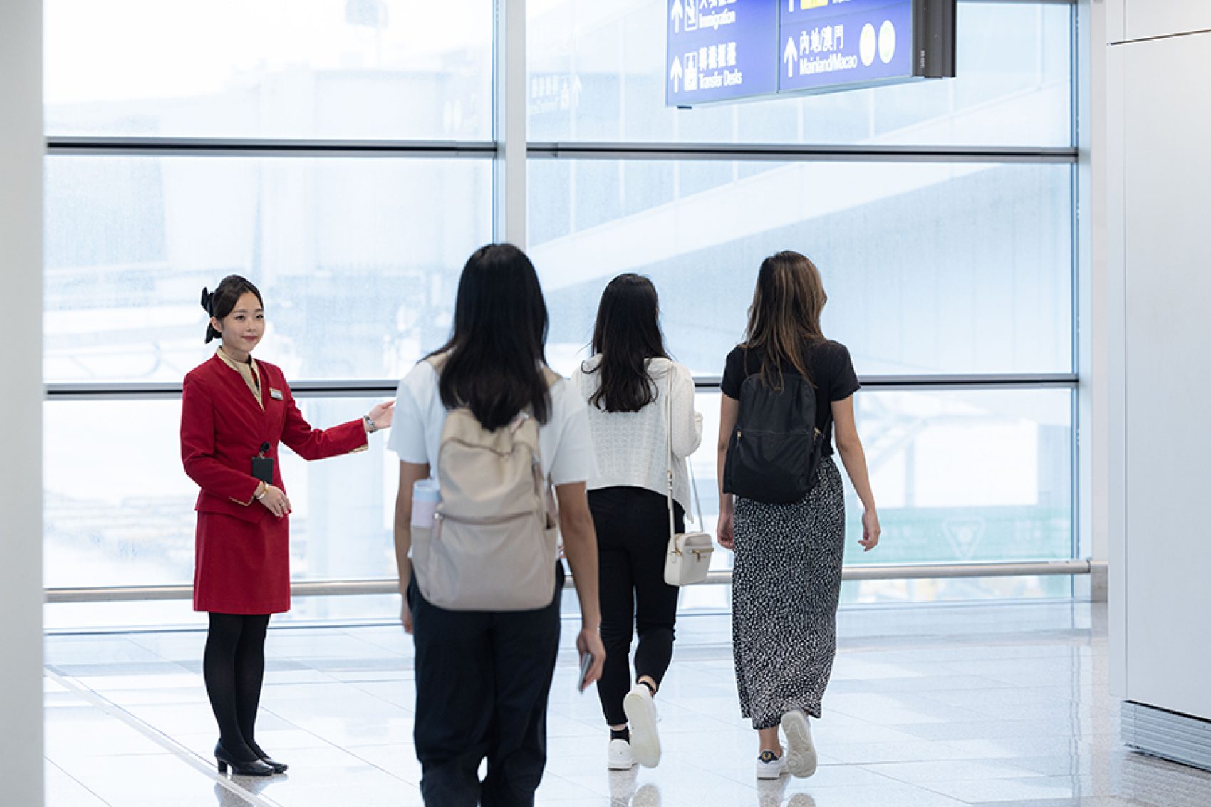 A group of passengers arriving at Hong Kong International Airport and being greeted by a Cathay Pacific flight attendant. 