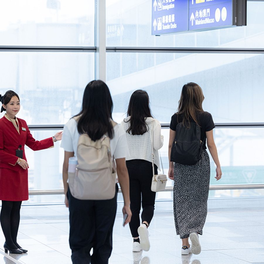 A group of passengers arriving at Hong Kong International Airport and being greeted by a Cathay Pacific flight attendant. 
