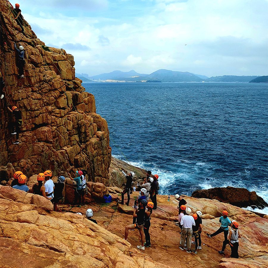 A group of people wearing safety gear and rock climbing on a cliff by the sea