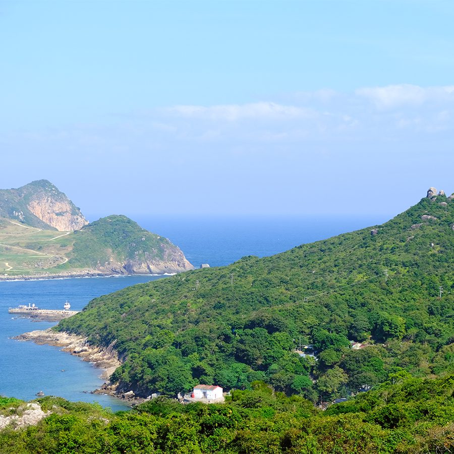 A scenic view of Hong Kong's green hillside by the seaside on a sunny day