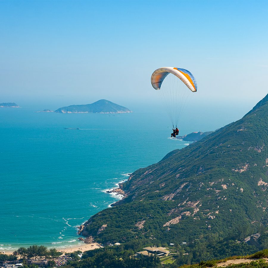 An aerial view of a person parasailing from a hilltop over the ocean on a clear day