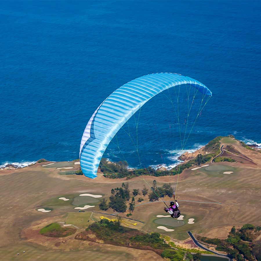 An aerial view of a person parasailing over a golf course near the ocean
