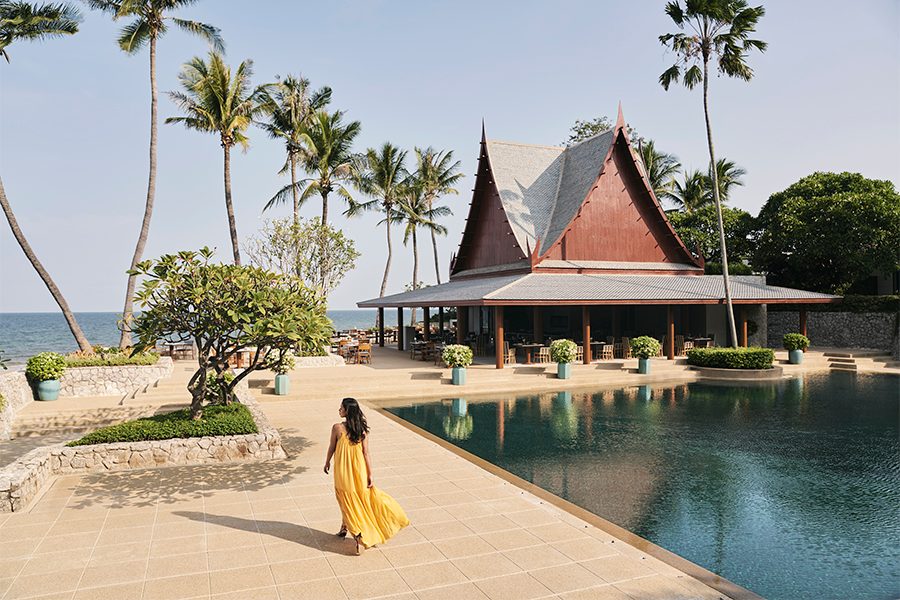 A woman in a long yellow dress walking by an outdoor pool at Chiva Som