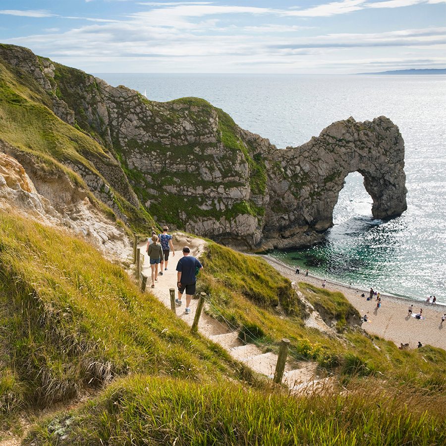 A group of people hiking down a hill along the coast next to a beach in Durdle Door, Dorset, England
