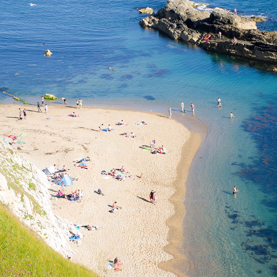 A crowd of people having fun at a small beach and in the blue waters in Durdle Door, Dorset, England 