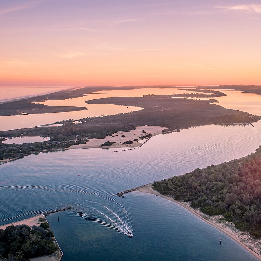 An aerial view of Gippsland Lakes surrounded by small lands and trees at sunset 
