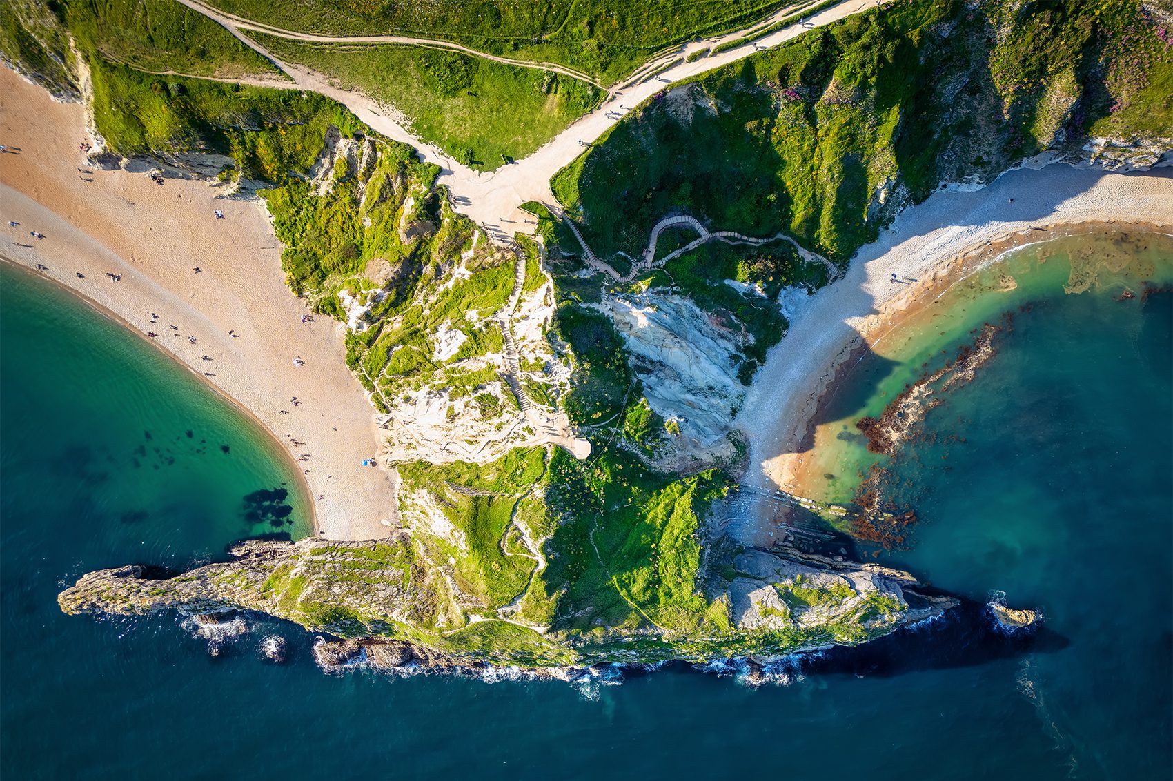 A top down aerial view of people lounging on a beach at a coastal cliff in Lulworth Dorset, England