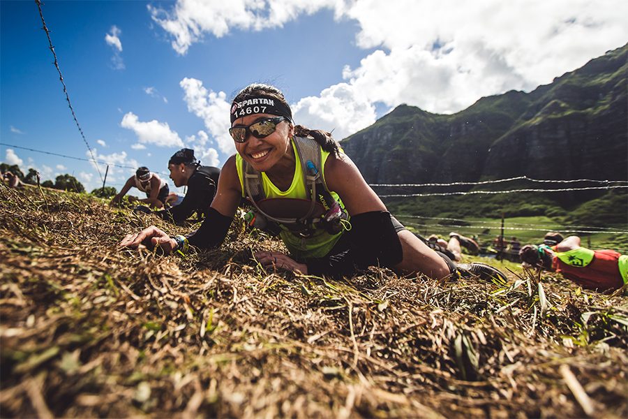 A group of men and women smiling crawling up a hill at a Spartan race