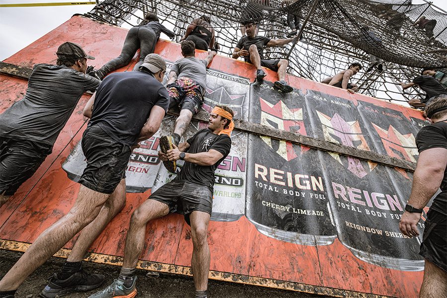 A group of people covered in mud climbing up the side of a tall wooden structure at Tough Mudder 