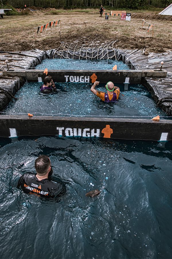 A group of people swimming and climbing an obstacle course at Tough Mudder