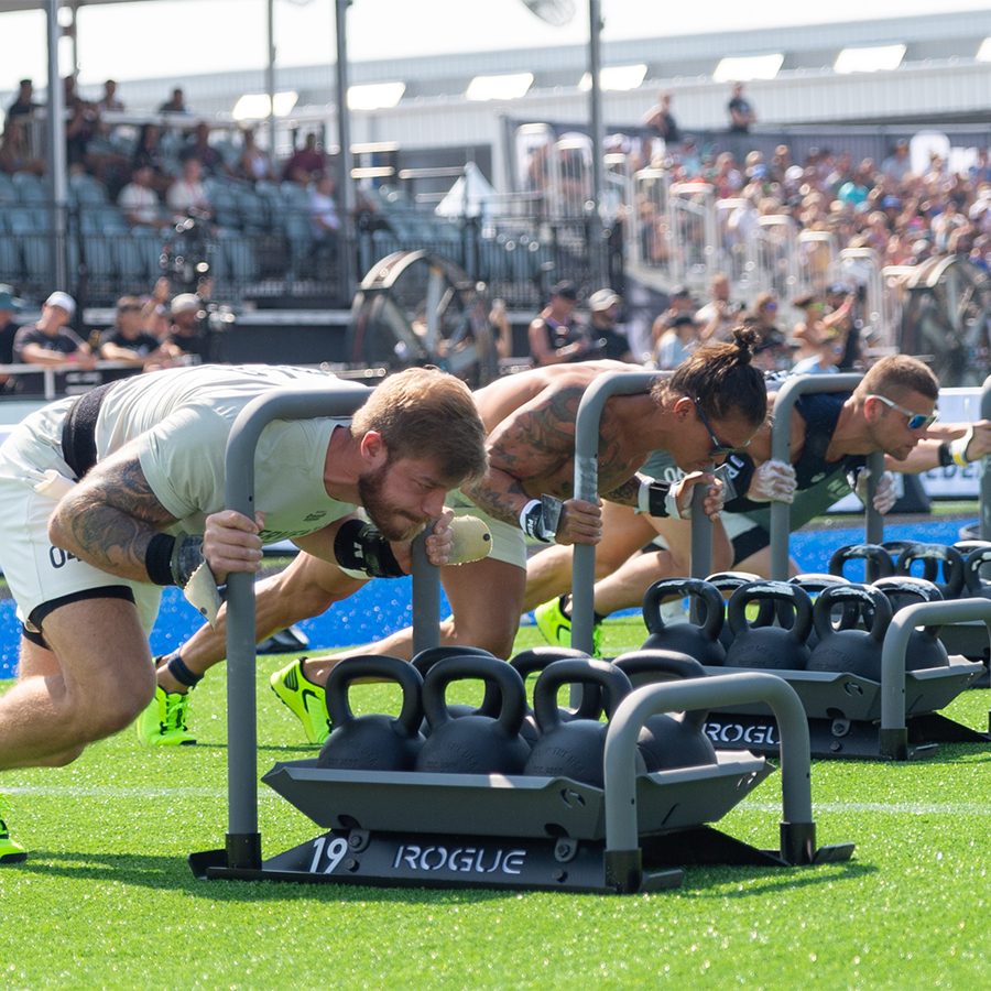 A group of men and women pushing a weighted sled across a field of grass at the CrossFit Game