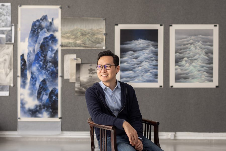 Chan Keng Tin sitting in front of a wall of his paintings