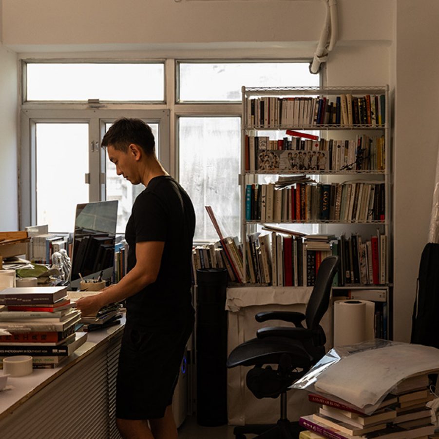 Artist Wai Pong Yu surrounded by stacks of books