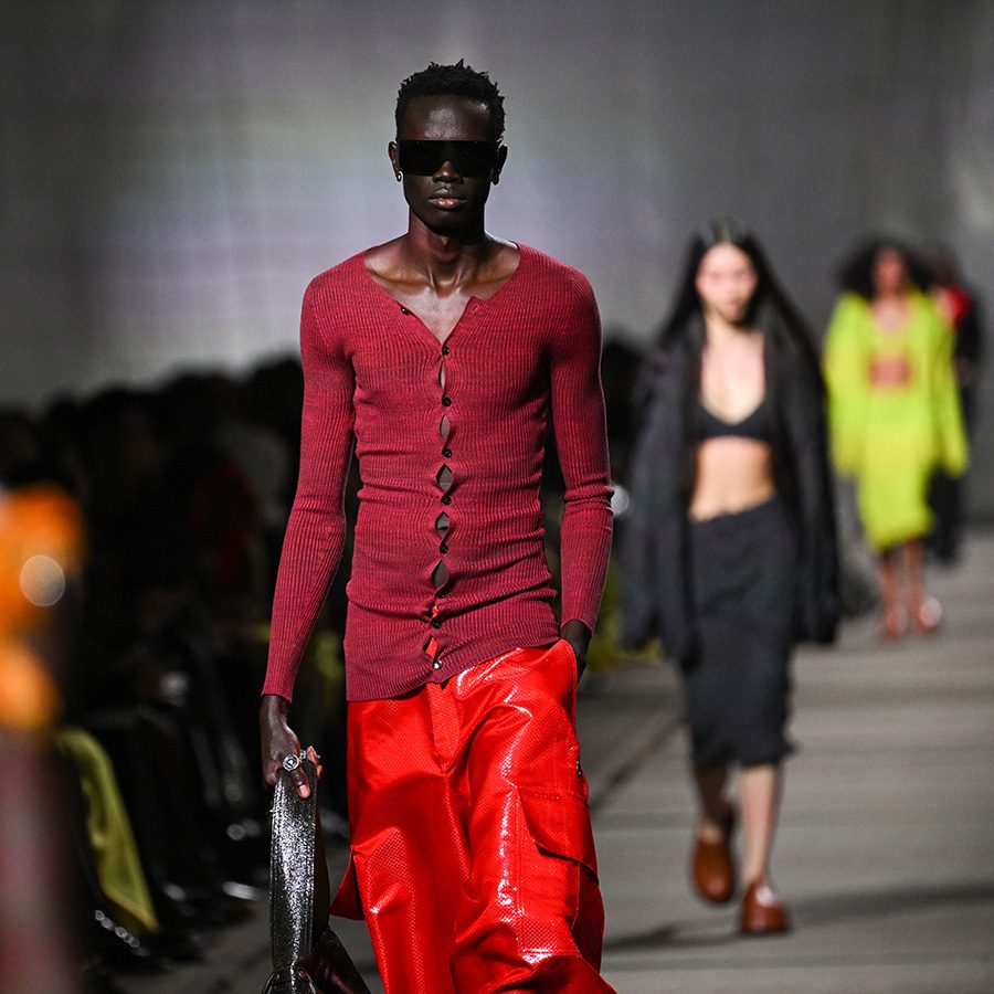 Male model wearing red top at a Alexander McQueen runway