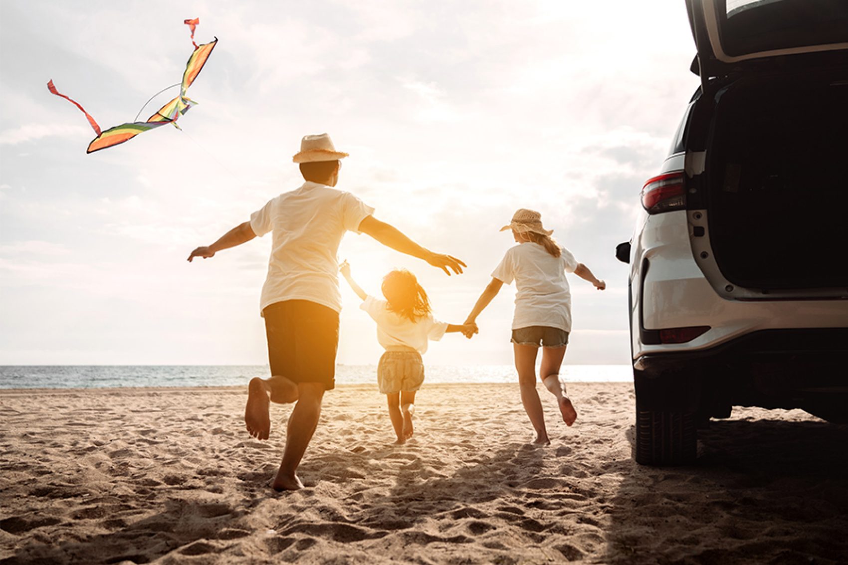 Family running on beach next to car