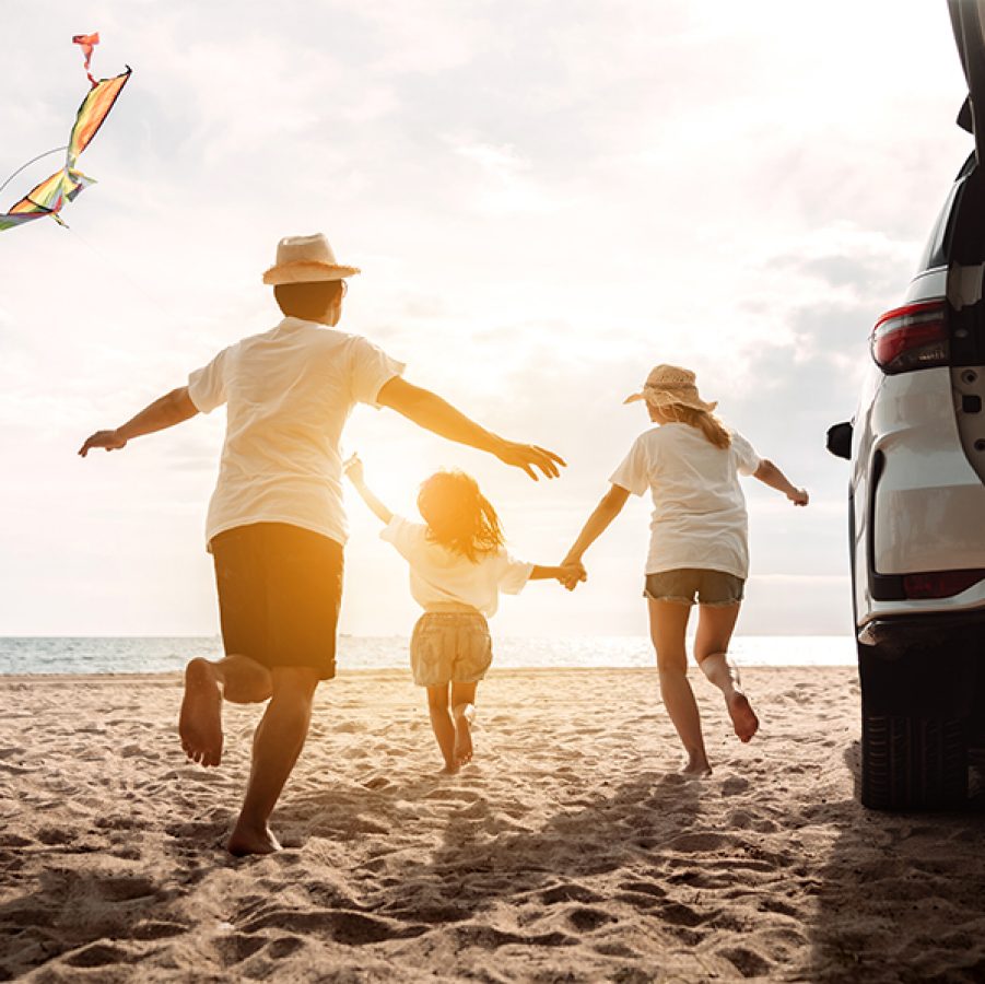 Family running on beach next to car