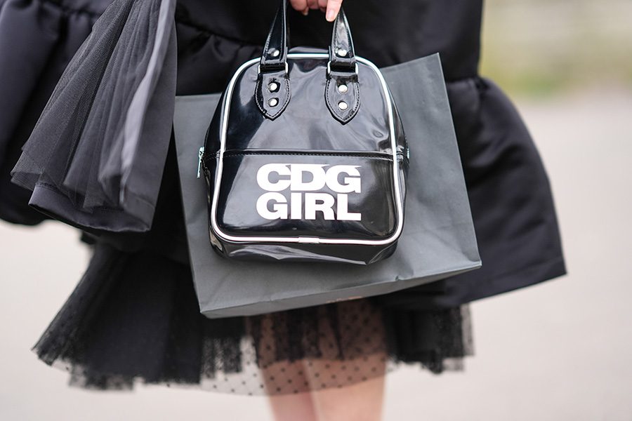 A woman is holding a shiny black handbag with 'CDG GIRL' printed in white letters