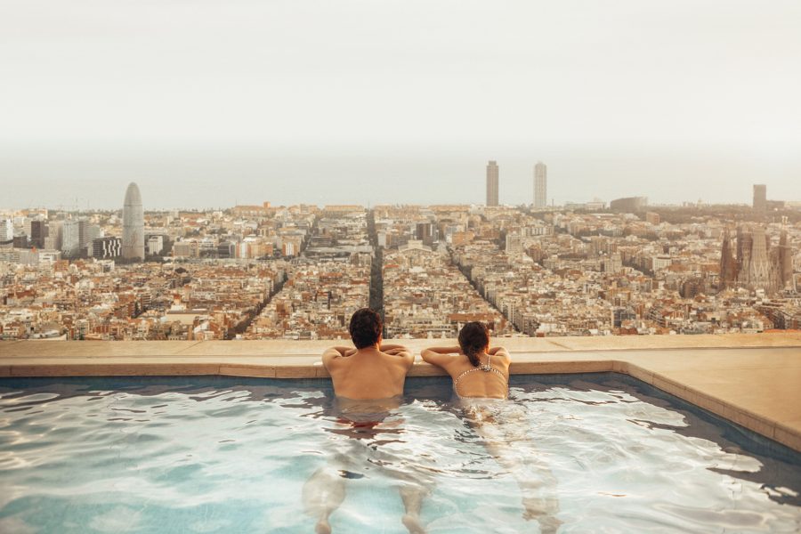 Man and woman in pool looking onto Barcelona skyline
