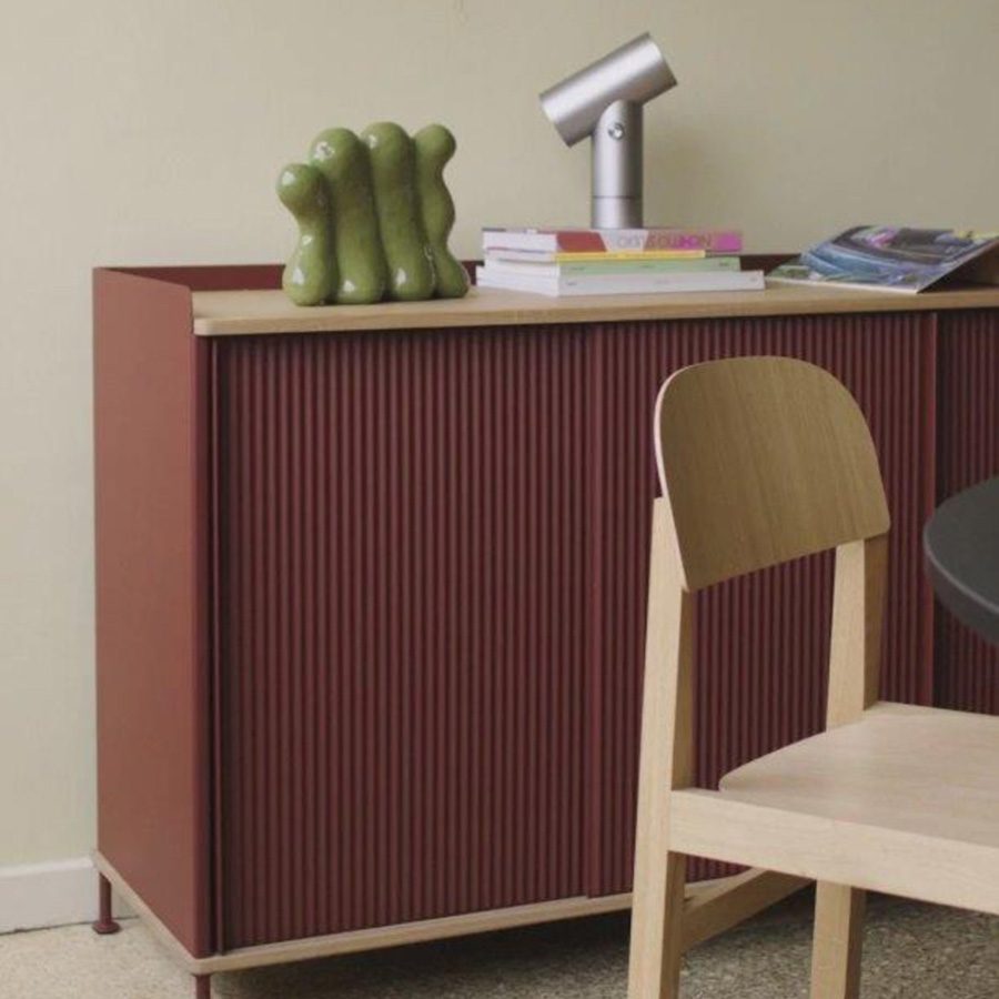 Enfold sideboard with books and a green sculptural object on top, next to a wooden chair.