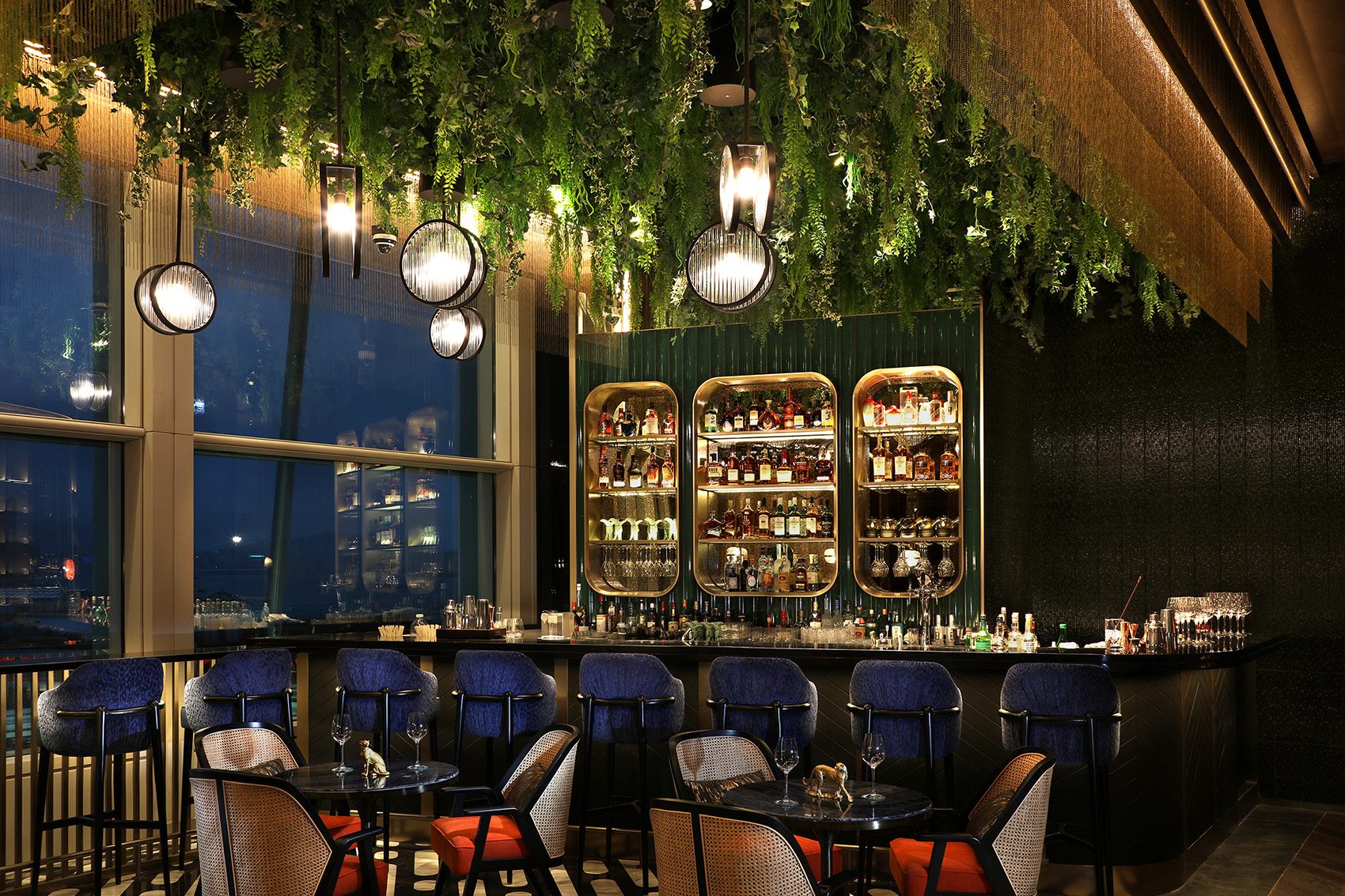 Chinesology bar interior with hanging greenery, modern lighting, and a well-stocked bar.