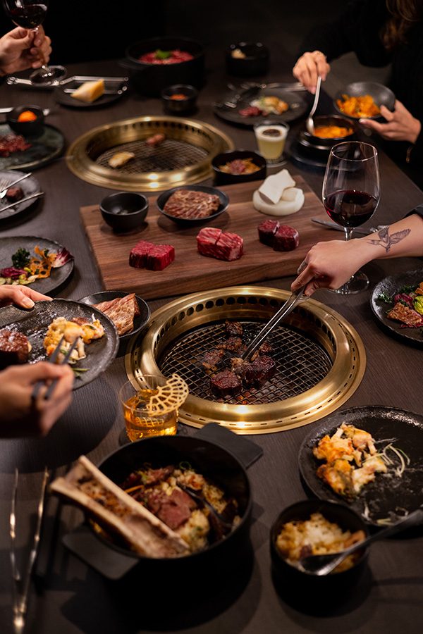 People gathering around a spread of dishes to grill meat at JJJ Korean Steakhouse