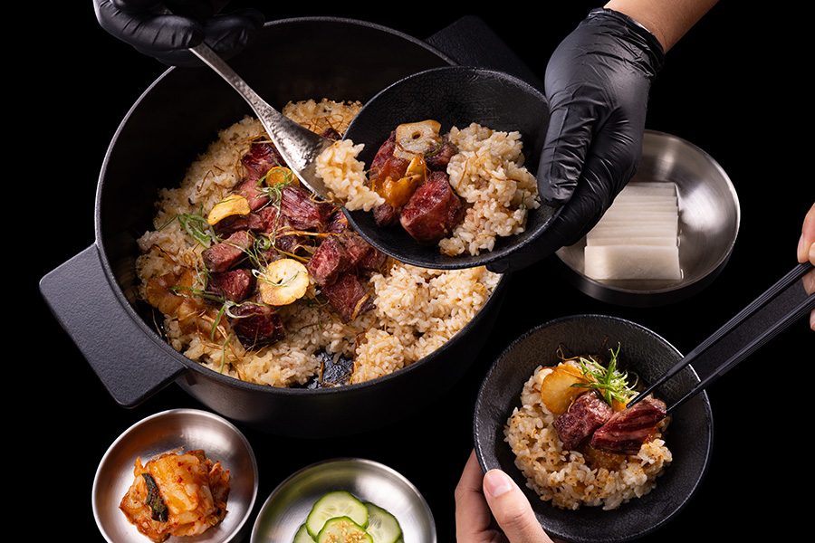 A person serving bowls of rice and meat being from a pot at JJJ Korean sharing food