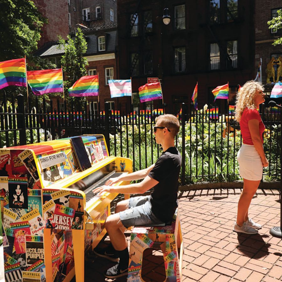 Man playing piano outdoors with surrounding rainbow flags