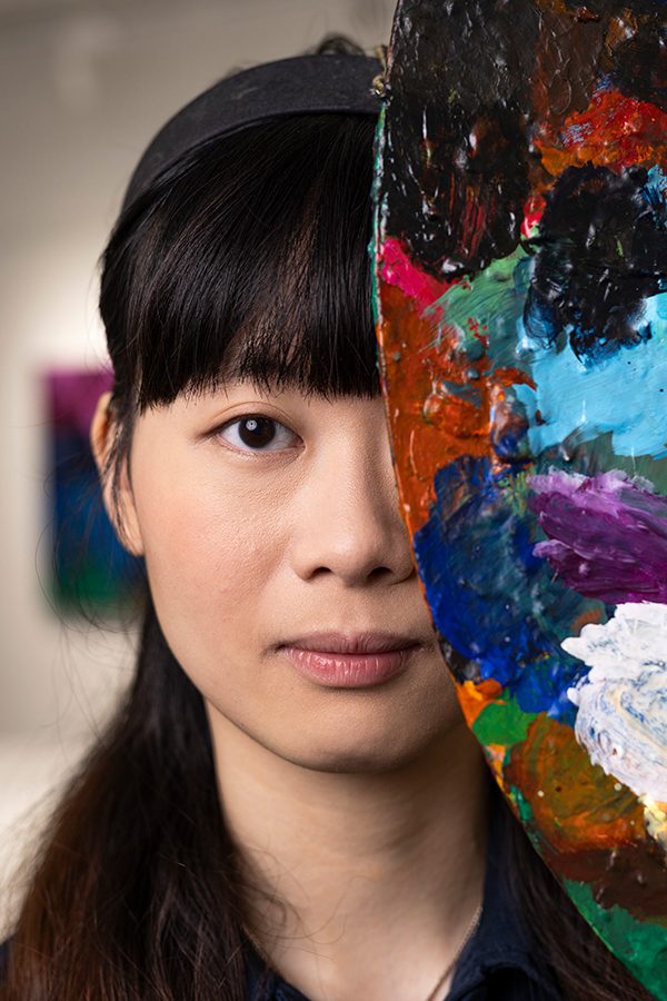 Elaine Chiu covering her half face using an artwork