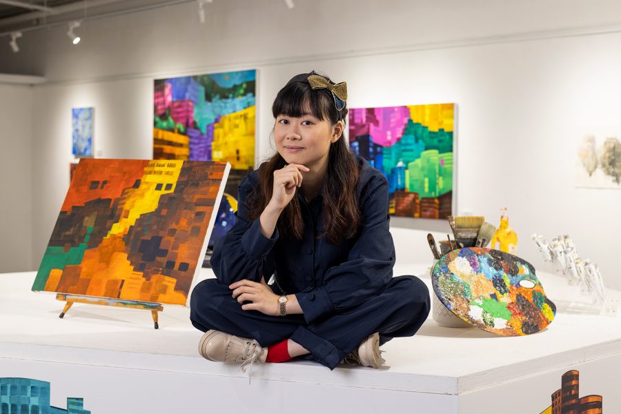 Elaine Chiu sitting on a white plinth surrounded by paintings and tools