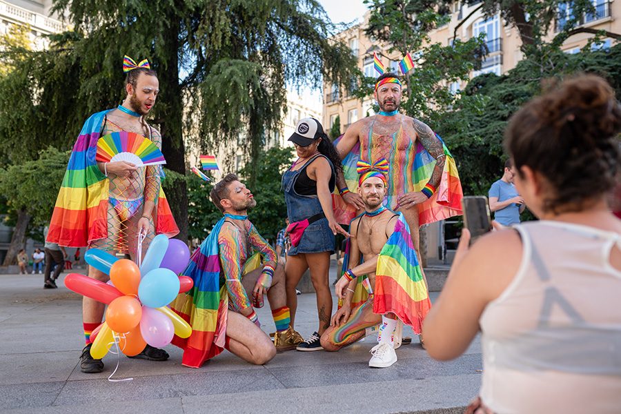 People with bright rainbow flags posing for a picture outdoors at a pride parade in Madrid, Spain