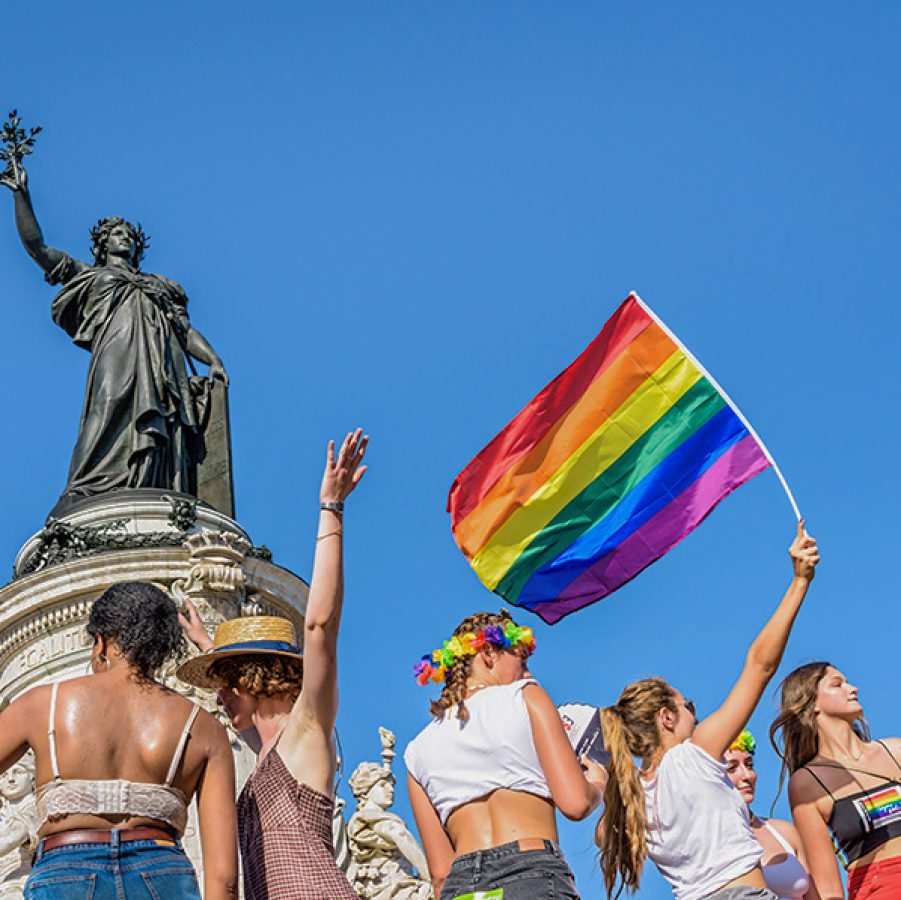 Six young women waving a rainbow flag high during pride parade in Paris, France