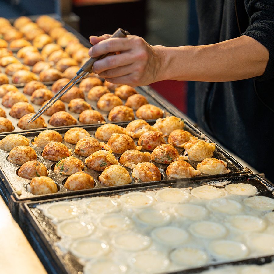 A man is grilling some Takoyaki at a food stall