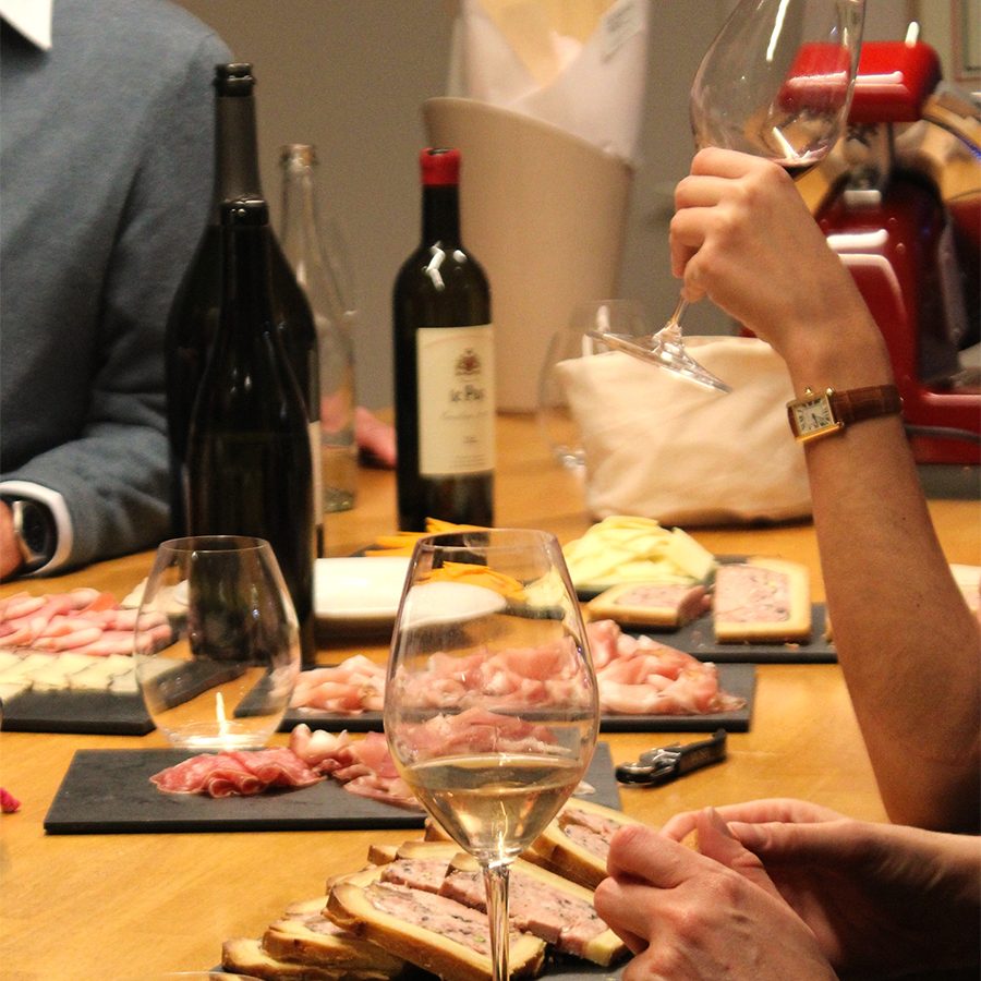A group of people having a wine tasting party with bottles of red wine and platters of cold cuts, cured meats and cheeses