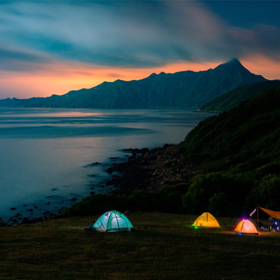 Tents lit up in front of the ocean and mountains at night