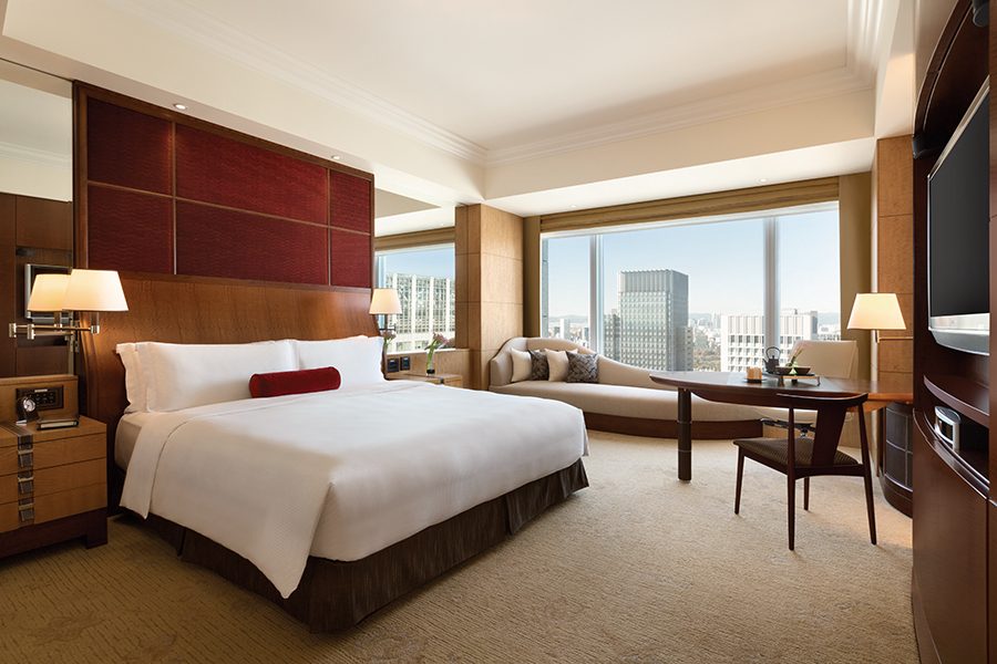 An image of the bedroom interior at Shangri-La Tokyo hotel with a view of the city during the day