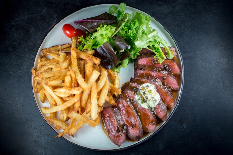 A plate of beef with fries and vegetables.