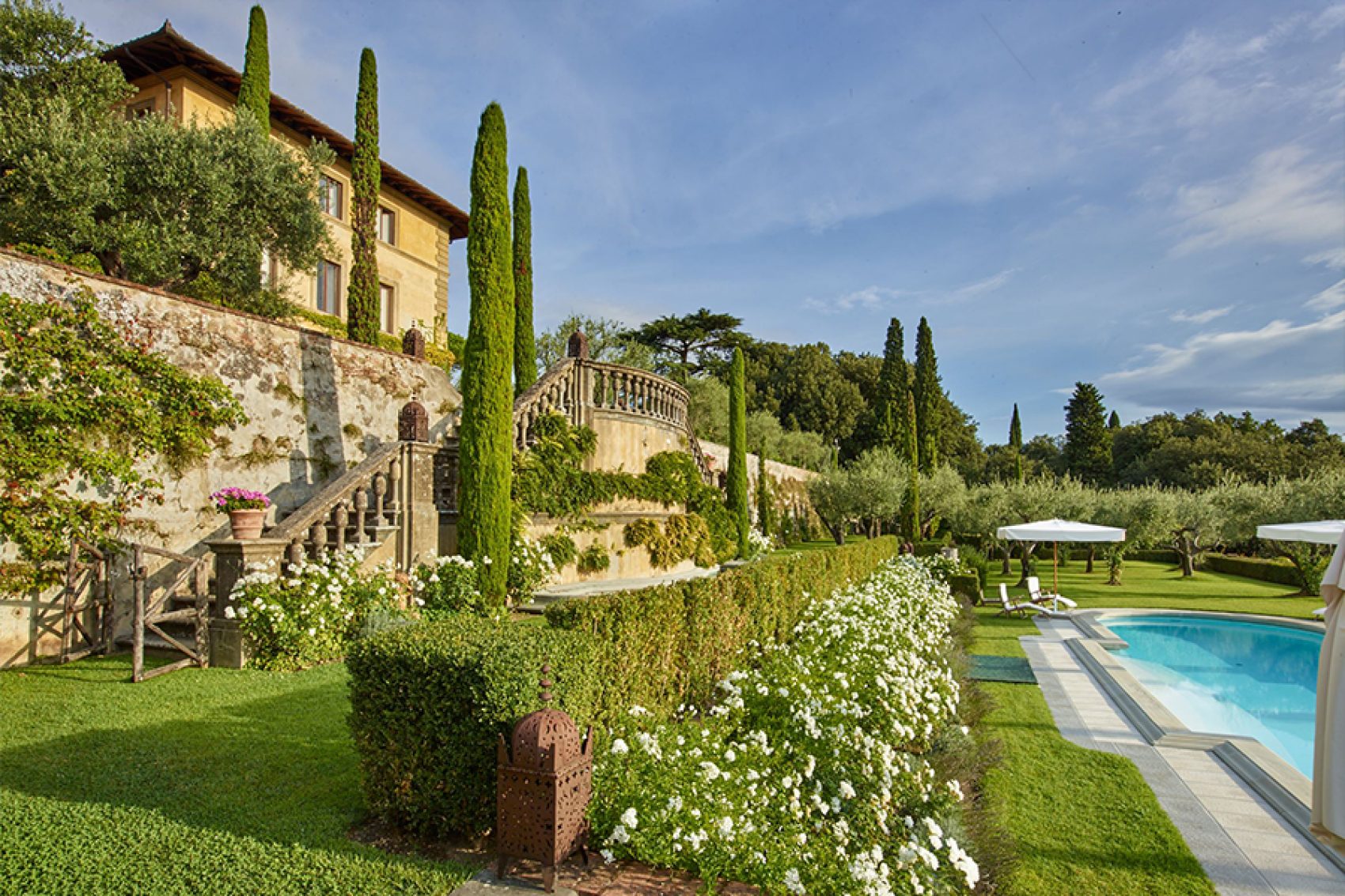 An outdoor view of the Il Palagio winery during the day with a garden and pool by the stairs