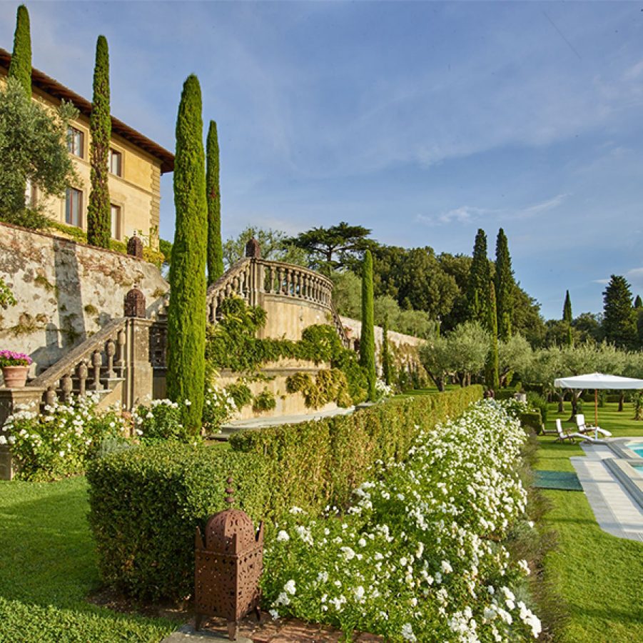 An outdoor view of the Il Palagio winery during the day with a garden and pool by the stairs