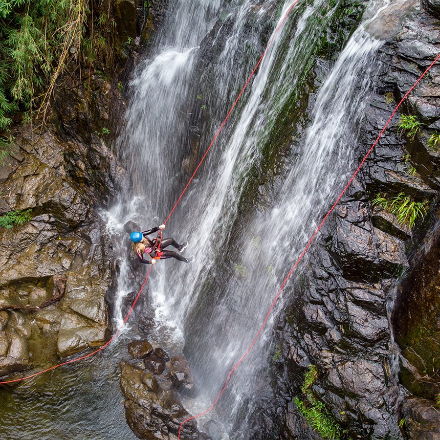 A man coasteering, rappelling down a waterfall and rocky cliff