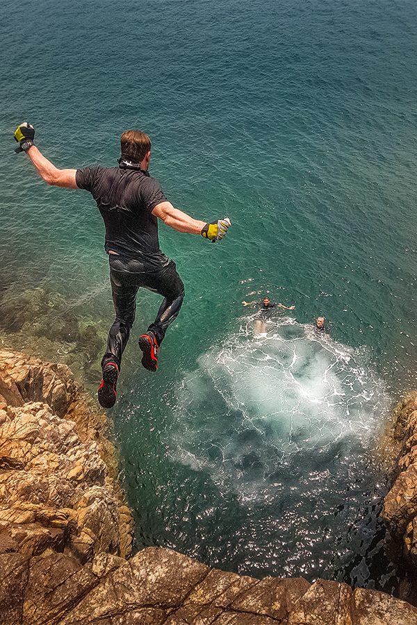 A man, jumping off a cliff and diving into the open sea during coasteering a adventure in Hong Kong