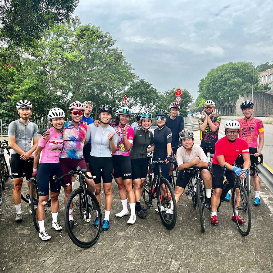 A group of cyclists from Rapha Hong Kong Clubhouse posing for a photo outdoors with their bikes in full cycling attire